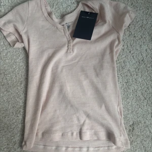 Randig rosa topp från Brandy Melville - Supersöt ljusrosa och vit randig topp från Brandy Melville. Modellen har korta ärmar, rund halsringning och knappar framtill. Helt ny med lappen kvar och aldrig använd💕