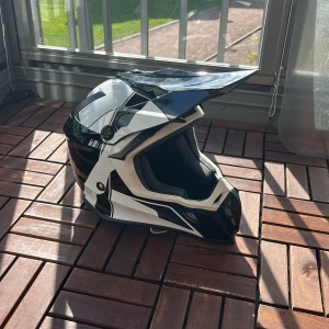 Svartvit motocrosshjälm M 57-58 - Snygg motocrosshjälm i svart, grå och vit med coola detaljer. Hjälmen har en skärm framtill med ventiler för bra luftflöde. Mycket lite använd, nytvättad, inga skador. ECE-godkänd. Kontakta vid intresse. 