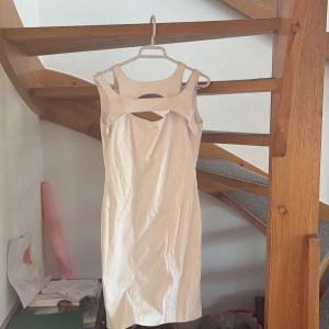 Vit satin klänning Guess by Marciano - Supersnygg vit kortklänning från Guess by Marciano. Klänningen är ärmlös med coola cut out-detaljer fram och v-ringning bak. Stängs med dragkedja och tryckknappar i nacken. Perfekt för dig som vill sticka ut med en stilren look.