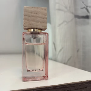 Rituals Fleurs de l'Himalaya parfym - Rituals Fleurs de l'Himalaya Eau de Parfum i en stilren, rektangulär glasflaska med ljusrosa ton och en snygg träkork. Flaskan rymmer 15 ml och har en lyxig känsla med guldiga detaljer vid halsen. Perfekt storlek att ta med i väskan.