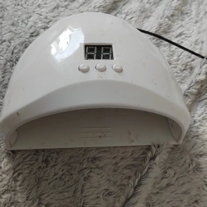Vit UV-lampa för naglar med timer - UV-lampa för naglar i vit plast med digital display och tre knappar för timer (30s, 60s, 90s). Lampan har USB-sladd för enkel anslutning och är perfekt för att härda gel- eller shellacklack hemma. Modern, kupolformad design. ( Sladden e lite trasig men funkar )