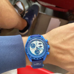Omega x Swatch blå MoonSwatch - Säljer en Omega x Swatch MoonSwatch Mission to the Super Blue Moonphase. Klockan är helblå med biokeramisk boett, blått textilband och vita detaljer. Snygg månfasedesign på baksidan och Omega-logga på bandet. Kommer med originalbox och tillbehör. Lite skrapor på glaset och boxen är lite trasig annars inga fel.😊