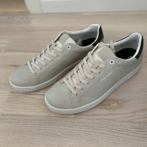 Beige sneakers från Björn Borg strl 43 - Stilrena sneakers från Björn Borg i beige med mörkgrön detalj på hälen. Skorna har snörning, rund tå och platt sula. Tillverkade i syntetmaterial med diskret logga på sidan. Perfekta för dig som gillar en clean och klassisk look. Helt oanvända och orginallåda finns.