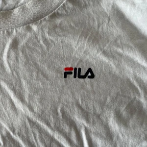 Vit FILA t-shirt i bomull XL - Vit t-shirt från FILA i storlek XL med klassisk logga broderad på bröstet. T-shirten har rund halsringning och korta ärmar. Tillverkad i mjuk bomull som är skön att bära hela dagen. Enkel och stilren design som funkar till det mesta.
