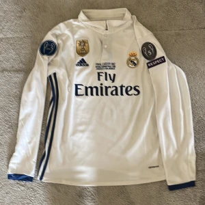 Real Madrid Ronaldo långärmad tröja - Säljer en långärmad Real Madrid fotbollströja från Adidas med Ronaldo 7 på ryggen. Tröjan är vit med blå detaljer, broderat klubbmärke, FIFA World Champions 2018-märke och Champions League-patchar. Materialet är lätt och andas, perfekt för fotboll eller samling.