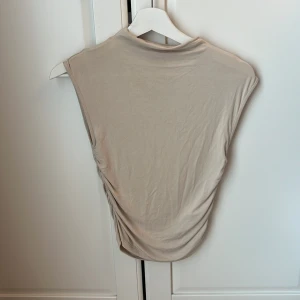 Beige soft touch topp från Gina Tricot - Säljer en beige ärmlös topp från Gina Tricot. Toppen har en tight passform och scrunch  längs sidorna🩷