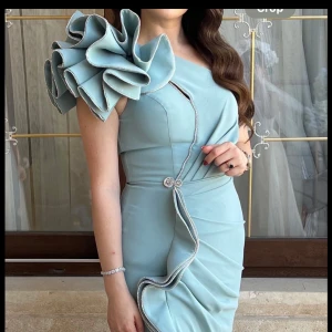 Ljusblå långklänning med volangärm - Superfin ljusblå långklänning med en axel och stor volangdetalj på axeln. Klänningen har en snygg slits framtill och dekorativa detaljer längs volangen. Perfekt för dig som vill sticka ut med en unik och elegant look. Den är använd en gång!