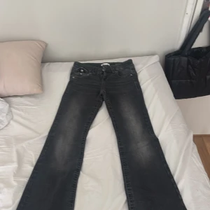 Svarta bootcut jeans Gina Tricot 146 - Snygga svarta bootcut jeans från Gina Tricot i storlek 146. Jeansen har slitna detaljer nertill, klassiska fickor med lock och knappar bak samt dragkedja framtill. Perfekta för dig som gillar en cool och avslappnad stil.