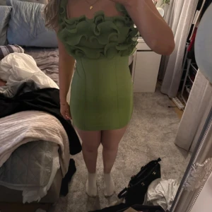 Grön kort klänning med volang - Supersöt grön kort klänning med volangdetaljer upptill och breda axelband. Tight passform som framhäver figuren och ger en trendig look. Perfekt för dig som vill sticka ut med en färgglad och unik stil. Onesize men skulle sagt att storleken är S/M