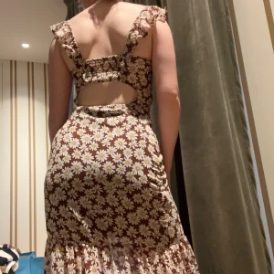 Brun långklänning med prästkragar - Superfin brun långklänning med vita och gula prästkragar, volangärmar och v-ringning. Klänningen har öppen rygg, slits framtill och smickrande passform. Perfekt för sommarens alla tillfällen!