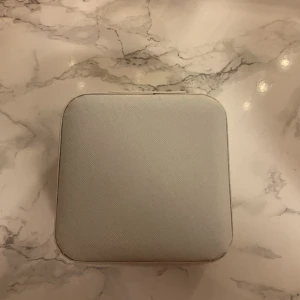 Vit smyckesväska med dragkedja - Snygg och stilren vit smyckesväska i fyrkantig form med dragkedja. Utsidan är i ett slätt material och insidan har fack för ringar, örhängen och andra smycken. Perfekt att ha med på resan eller för att hålla ordning hemma.