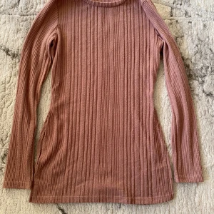 Rosa ribbad långärmad tröja - Supersnygg långärmad tröja i en dämpad rosa nyans. Tröjan är ribbad med vertikala ränder och har en slits på sidan som ger en extra detalj. Perfekt till jeans eller kjol för en chill och trendig look.