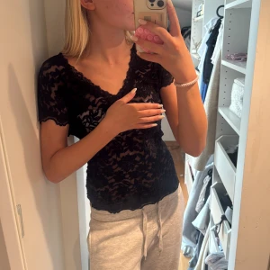 Svart spetsblus med v-ringning - Säljer en svart, genombruten spetsblus med v-ringad hals och korta ärmar. Blusen har fina spetsdetaljer längs kanterna och sitter tight mot kroppen. Perfekt för dig som gillar en feminin och trendig look.