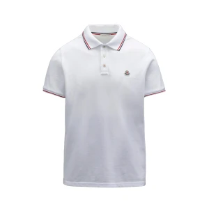 Vit Moncler pikétröja med logga - Vit pikétröja från Moncler med klassisk krage, knäppning framtill och diskret logga på bröstet. Röd och blå rand på krage och ärmslut ger en clean och sportig vibe. Perfekt till jeans eller shorts.