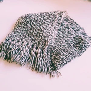 Grönvit stickad halsduk med fransar - En chunky stickad halsduk i grönt och vitt med tvinnat mönster och långa fransar i ändarna. Perfekt för kalla dagar när du vill ha något riktigt mysigt och stilrent runt halsen.  Helt & fint skick