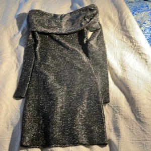 Glittrig offshoulder klänning H&M XS - Supersnygg kort glittrig klänning från H&M Divided i svart med silverglitter. Offshoulder-modell med lång ärm och tight passform som sitter perfekt för en kväll ute. Materialet är stretchigt och skimrar i ljuset. Perfekt för dig som vill sticka ut! Passar bra på nyår eller någon annan fest!