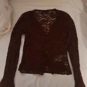 Vinröd spetskofta med knappar - Säljer en vinröd, transparent spetskofta från Gina Tricot. Koftan har lång ärm, v-ringning och dekorativa knappar framtill. Den är croppad och har ett romantiskt, detaljerat spetsmönster som ger en snygg och trendig look.