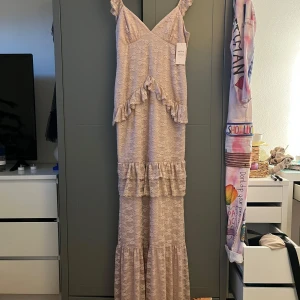 Ljusrosa spetsklänning från Nelly - Romantisk långklänning i ljusrosa spets från Nelly med volangdetaljer och v-ringning. Klänningen har smala axelband och flera lager volanger längs kjolen. Nyspris 900, mitt pris 600. DEN ÄR ALDRIG ANVÄND MED PRISLAPPEN KVAR. Föreslå gärna ett pris om du vill😊