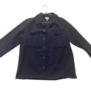 Mörkblå overshirt från H&M - Stilren mörkblå overshirt från H&M med klassisk krage, knäppning framtill och två bröstfickor. Jackan har lång ärm och en rak, avslappnad passform. Perfekt att slänga över en hoodie eller t-shirt för en chill look.