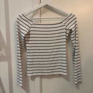 Randig långärmad topp offshoulder - Snygg vit långärmad topp med svarta horisontella ränder och offshoulder-skärning. Perfekt för dig som gillar en enkel men trendig stil. Mjuk och skön bomullskänsla, passar till både jeans och kjol.