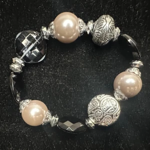 Chunky Y2K armband med stora pärlor i svart champagne & silver - Retro - 90-tal - 00-tal - Äkta vintagearmband från sent 90-tal/tidigt 2000-tal i klassisk Y2K-stil. Elastiskt med stora pärlemorskimrande pärlor (upp till 2 cm), facetterade svarta stenar och rikt dekorerade metallpärlor i silvrig finish. Mått: ca 17 cm. Inropat på auktion bland äldre bijouterier – perfekt för dig som vill ha ett original från perioden.  Prutning accepteras inte, men jag erbjuder gärna rabatt vid köp av flera saker. Jag rensar smyckesskrin och garderob – passa på att kika på mina andra annonser också!  