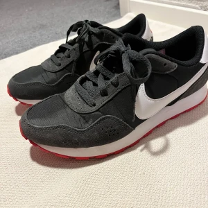 Svarta Nike sneakers med röd sula - Snygga svarta nike sportskor. Använda några gånger men säljer då dem va lite för små. Svarta med vita och röda detaljer 