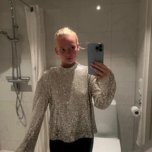 Glittrig silvertröja med paljetter - Superglittrig långärmad tröja i silver med massor av paljetter. Tröjan har en rak passform, hög hals och vida ärmar. Perfekt för dig som vill sticka ut och glänsa på nästa fest eller event. Helt ny. Inköpspris 439kr