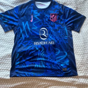 Atlético Madrid blå Nike fotbollströja - Snygg Atlético Madrid fotbollströja från Nike i olika blå nyanser med grafiskt mönster.  Tillverkad i lätt och ventilerande polyester, perfekt för match eller träning. Fick den som present och är splitterny! Storlek XL men passar också L.
