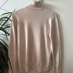 Beige polotröja från Zara  - Säljer en fin beige polotröja från Zara i mjukt material. Tröjan har långa ärmar och söta guldfärgade knappar vid ärmsluten. Endast använd ett fåtal gånger! 