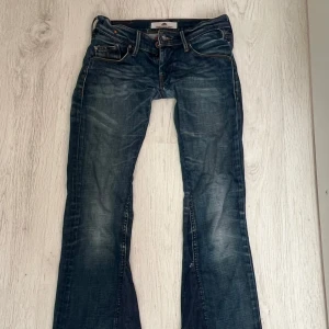 Blå bootcut jeans från Fornarina - Snygga blå jeans från Fornarina med bootcut passform och coola slitningar. Klassiska femficksdetaljer, kontrastsömmar och läderpatch bak. Tillverkade i bomull med lite stretch för skön passform. Perfekta för dig som gillar en avslappnad men trendig look.