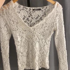 Vit spetsblus från Gina Tricot - Supersnygg vit blus i spets från Gina Tricot med blommigt mönster. V-ringad och figurnära passform med långa ärmar. Helt nytt skick