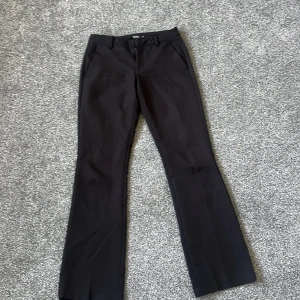 Svarta bootcut kostymbyxor - Snygga svarta kostymbyxor med bootcut-snitt och klassisk dragkedja samt hyska.En av knapparna har gått av men de går fortfarande att stänga med en andra
