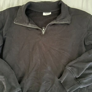 Svart half zip tröja från Kappahl - Svart långärmad tröja från Kappahl med ribbad krage och muddar. Tröjan har en half zip-dragkedja framtill och är gjord i mjukt bomullsmaterial. Perfekt för chill dagar och enkel att matcha med jeans eller mjukisbyxor.