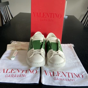 Valentino Garavani Open sneakers vit/grön - Snygga Valentino Garavani Open sneakers i vitt skinn med grön panel och ikoniska nitar på hälen. Klassisk rund tå, platt sula och snörning. Kommer med originalpåse och box. Perfekta för dig som vill sticka ut med lyxig streetstyle.