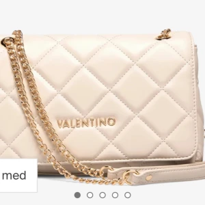 Beige quiltad axelväska Valentino - Snygg beige axelväska från Valentino med quiltad design och guldfärgad kedja. Väskan har en stilren look med logga framtill och är tillverkad i skinnimitation. Perfekt för dig som vill ha en trendig och elegant accessoar.