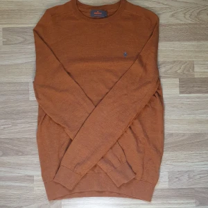 Stickad Morris tröja - Snygg stickad tröja från Morris i storlek L, tillverkad i 100% merinoull. Tröjan har rund hals och ett litet broderat emblem på bröstet. Perfekt för dig som gillar klassisk stil med en modern twist och vill ha något mjukt och bekvämt. Titta sista bilden för pytteliten skavanker