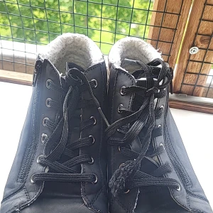 Svarta boots med foder och dragkedja - Svarta boots med snörning, dragkedja på sidan och vit sula. Insidan är fodrad med mjukt, vitt teddyfoder för extra värme. Baksidan har en metallic-detalj i brons. Perfekta för kyliga dagar och snygga till jeans.