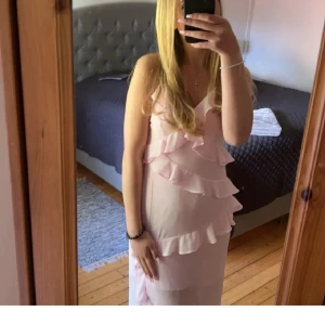 Ljusrosa långklänning med volanger - FINNS ÄVEN PÅ MIN VINTED skriv vid intresse Säljer en superfin ljusrosa långklänning med v-ringad hals och tunna axelband. Klänningen har flera lager med volanger framtill som ger en romantisk och flowy känsla. Materialet är lätt och känns luftigt, perfekt för varmare dagar eller speciella tillfällen.