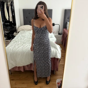 Gina Tricot blommig långklänning - Supersöt långklänning från Gina Tricot. Marinblå botten med vitt blommigt mönster, figurnära passform och snygg slits framtill. Perfekt för dig som gillar en feminin och trendig look. Materialet är mjukt och lätt. Köptes ett tag sen men kom nästan aldrig till användning och säljs inte mer🌸