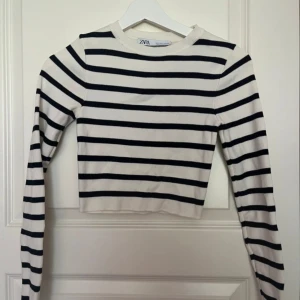 Randig croppad tröja från Zara - Säljer en croppad långärmad tröja från Zara i storlek S. Tröjan är vit med svarta horisontella ränder och har en rund halsringning. Materialet är mjukt och ribbat, perfekt för dig som gillar en chill och stilren look.