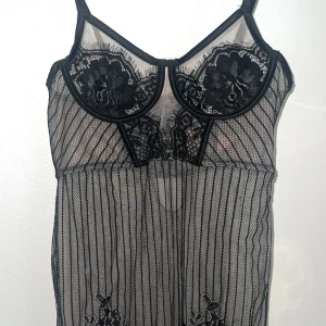 Nattklänning - Säljer en svart nattklänning med tunna axelband, genomskinligt mesh-tyg och dekorativa spetsdetaljer över bysten. Nattklänning har vertikala ränder och en liten öppning framtill för extra edge. Helt oanvänd. Kan ses i Stockholm samt posta. Pris kan diskuteras. ❤️