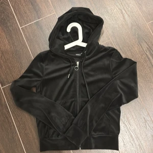 Svart velour hoodie från Gina Tricot - Svart hoodie i mjuk velour från Gina Tricot, storlek S. Tröjan har huva, långa ärmar och en snygg dragkedja med ringdetalj framtill. Perfekt för chill dagar och när du vill ha en skön och stilren look.