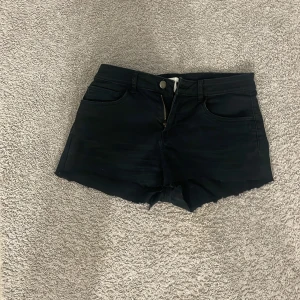 Svarta jeansshorts med rå kant - Svarta jeansshorts med klassisk femficksdesign och rå, avklippt kant nedtill. Modellen har dragkedja och knapp framtill samt bälteshällor. Perfekta för dig som gillar en enkel och edgy stil på sommaren.