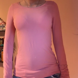 Rosa långärmad topp - Säljer en enkel och snygg rosa långärmad topp med rund hals. Modellen är figurnära och passar perfekt till jeans eller kjol. Materialet känns mjukt och stretchigt, vilket gör den skön att bära hela dagen.