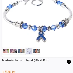 Silvrigt armband  med blå och vita pärlor, cancer fonden - Unikt silvrigt armband med kedja och hängande blå och vita pärlor. I mitten finns ett berlockformat band som ger extra karaktär. Perfekt för dig som gillar detaljer och vill sticka ut med coola accessoarer. 