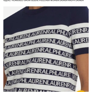 Randig stickad tröja Ralph Lauren - Snygg stickad tröja från Ralph Lauren med korta ärmar. Tröjan är marinblå och vit med randigt mönster och logotypen 'LAUREN RALPH LAUREN' upprepad över hela plagget. Rund halsringning och ribbade muddar ger en klassisk vibe.