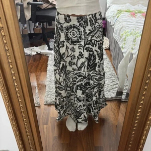 Svartvit långkjol med blommigt mönster - Säljer en svartvit långkjol med blommigt mönster. Har inte använt på ett tag och det är därför jag säljer den. Såhär sitter den på mig och jag är ca 160 cm lång ❤️