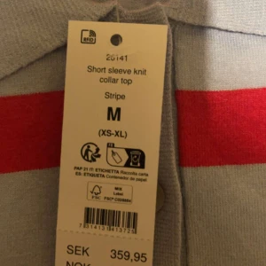 Randig stickad polotopp i rött och ljusblått - Säljer en kortärmad stickad polotopp med breda röda och ljusblå ränder. Toppen har klassisk krage och ribbade kanter. Perfekt för dig som gillar retrovibbar och vill sticka ut med färg. Supermjuk och skön att bära.