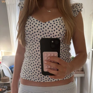 Prickig vit blus med volangaxlar - Supersöt blus i vit med mörkblå prickar och volangdetaljer på axlarna. Toppen är perfekt till sommaren och hör av er om ni har frågor!!💗