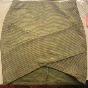 Olivgrön ribbad omlottkjol - Snygg olivgrön kortkjol med ribbad struktur och omlott-detalj framtill. Kjolen har en tight passform och är perfekt för dig som gillar en stilren men ändå trendig look. Passar till både sneakers och boots.